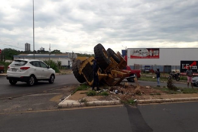 Pá carregadeira cai de caminhão e fica tombada em canteiro